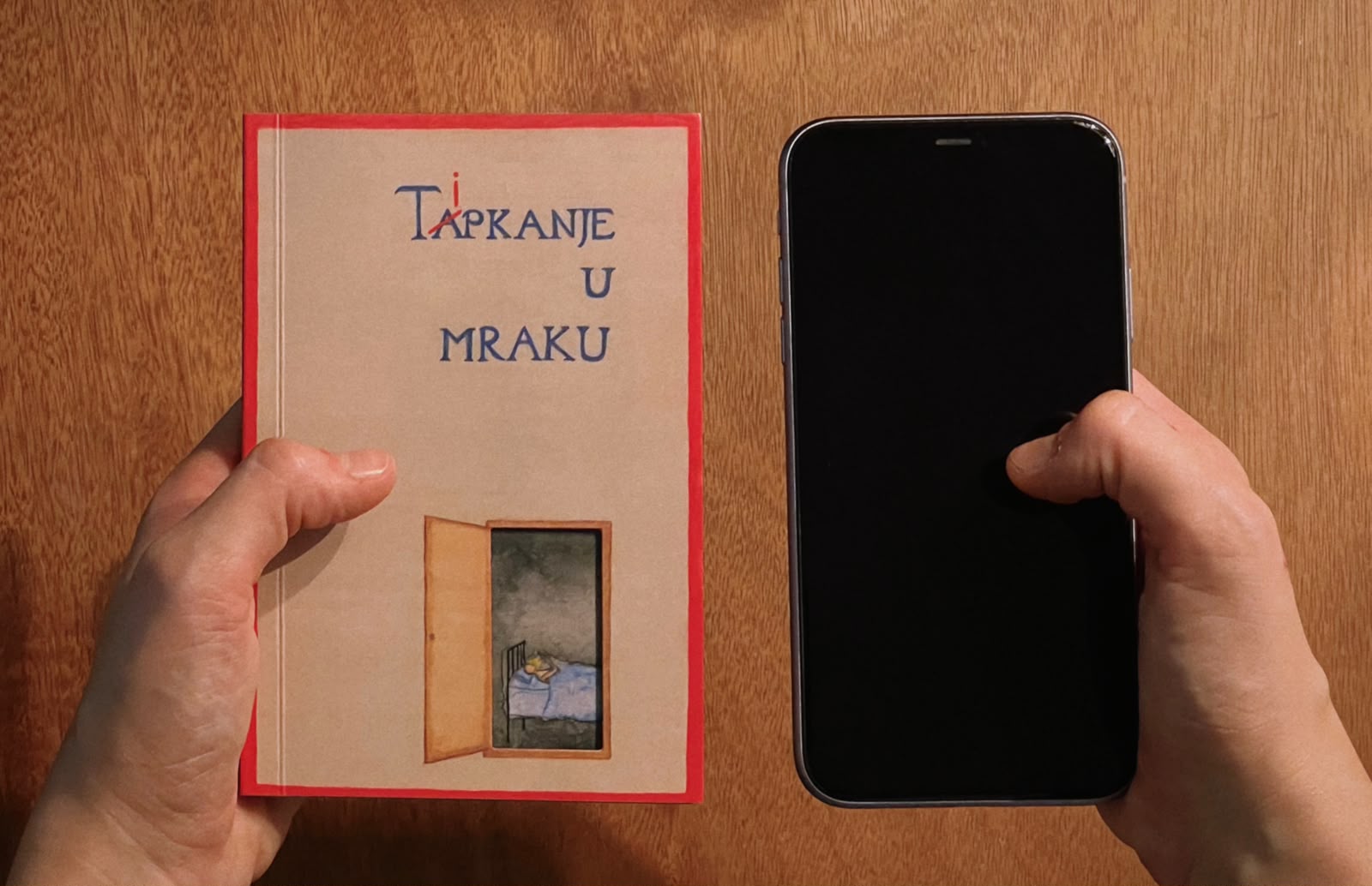 Ruke koje drže slikovnicu Tipkanje u mraku i mobitel